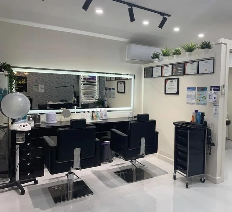 Two-station salon interior — black styling chairs, full-width LED mirror, product trolley, framed qualification certificates, white tile floor