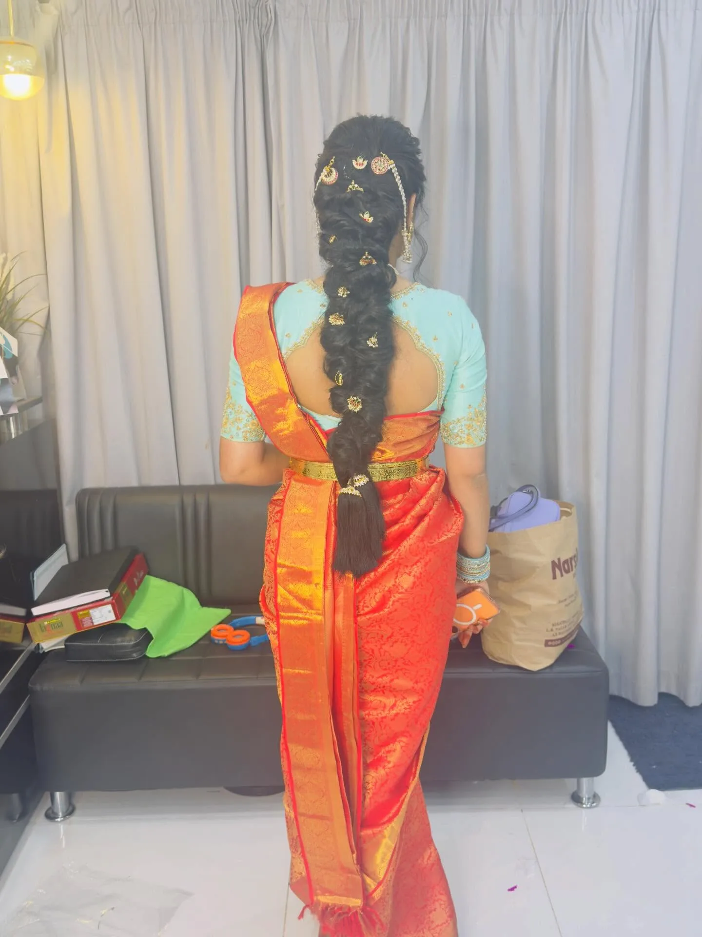 Rear view of long ornamented bridal braid with jasmine garland, orange and red saree, in-salon