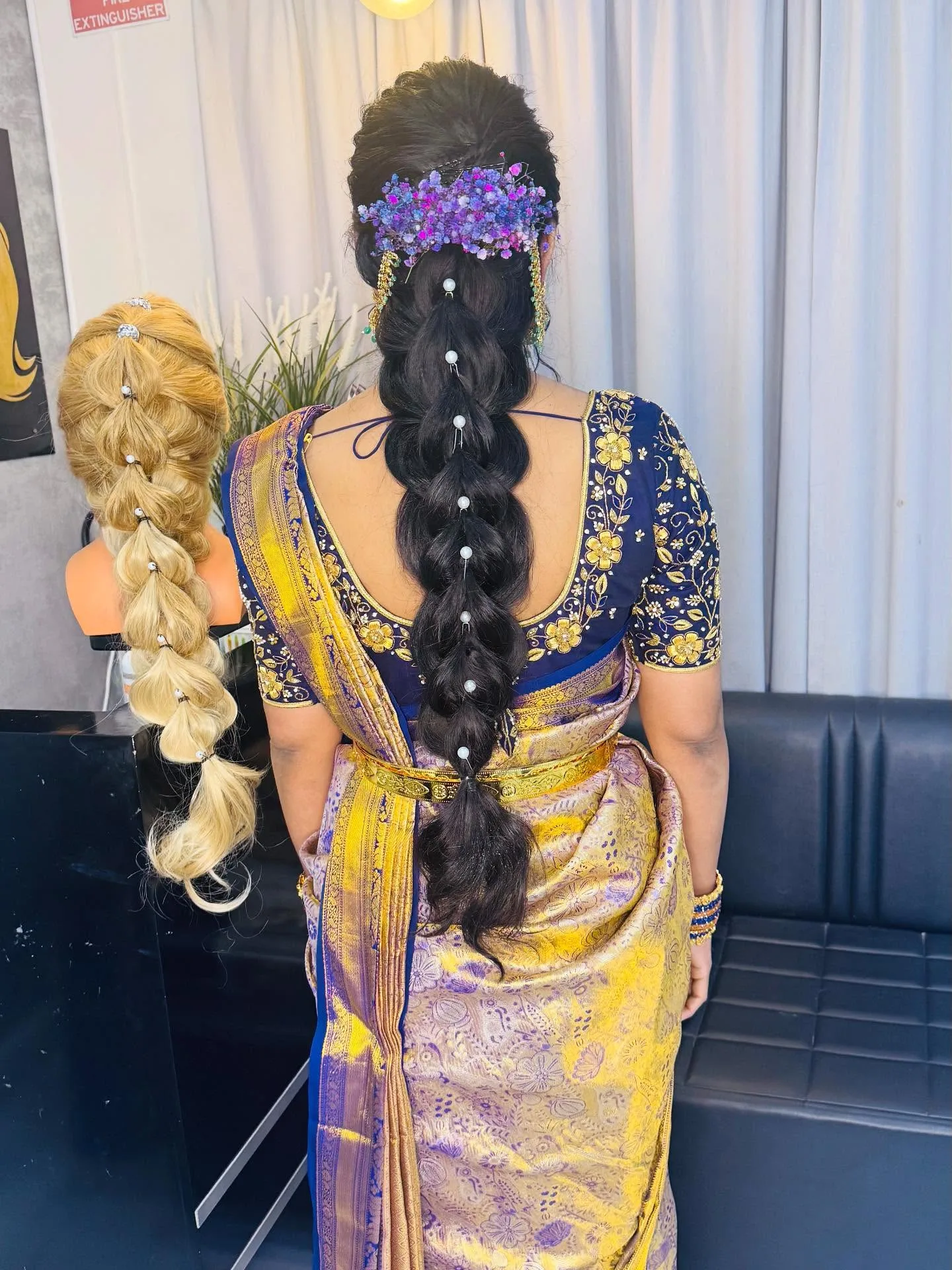Rear view of pearl-pinned bridal braid with blue and pink babys-breath, navy gold saree, in-salon