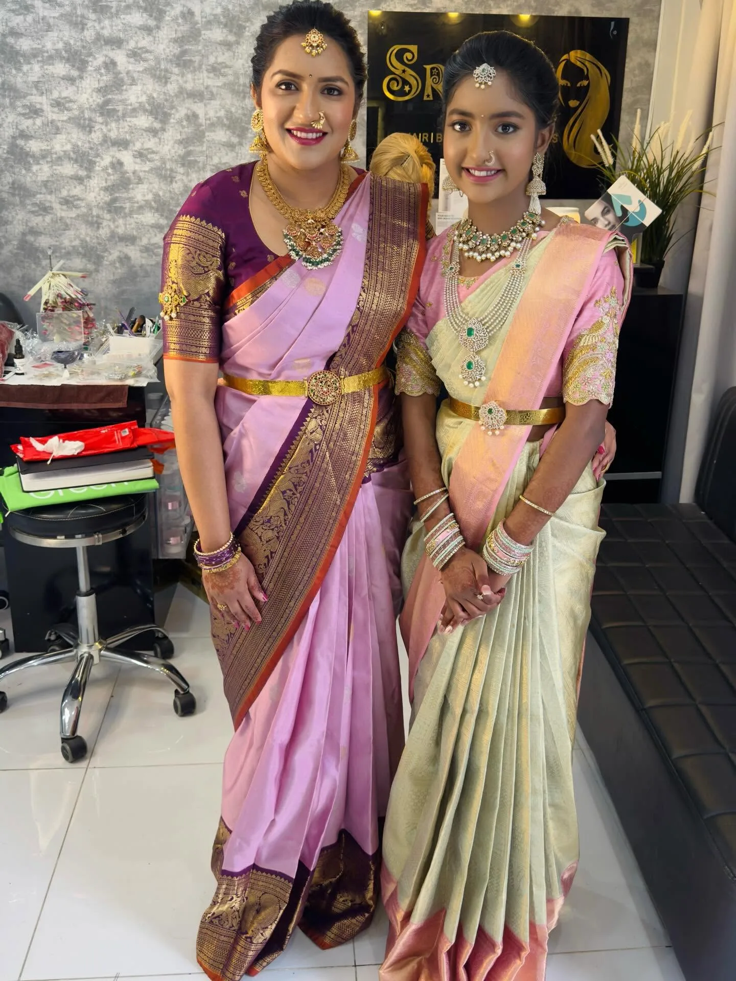 Two clients in pink sarees and temple jewellery standing in the salon by the Srijams plaque