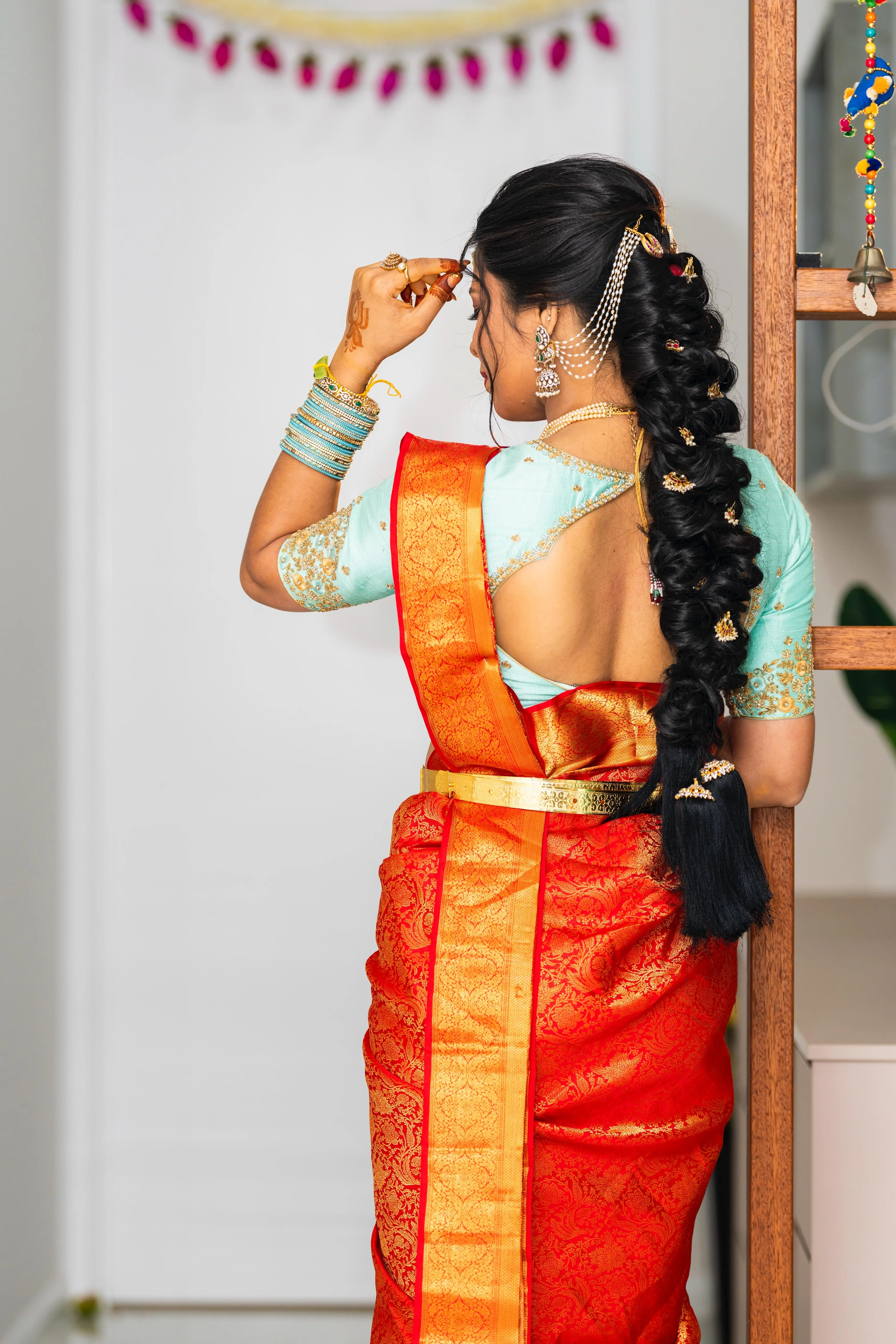 Rear view of long gold-jewelled fishtail bridal braid, red-gold kanjivaram and teal blouse, festive venue