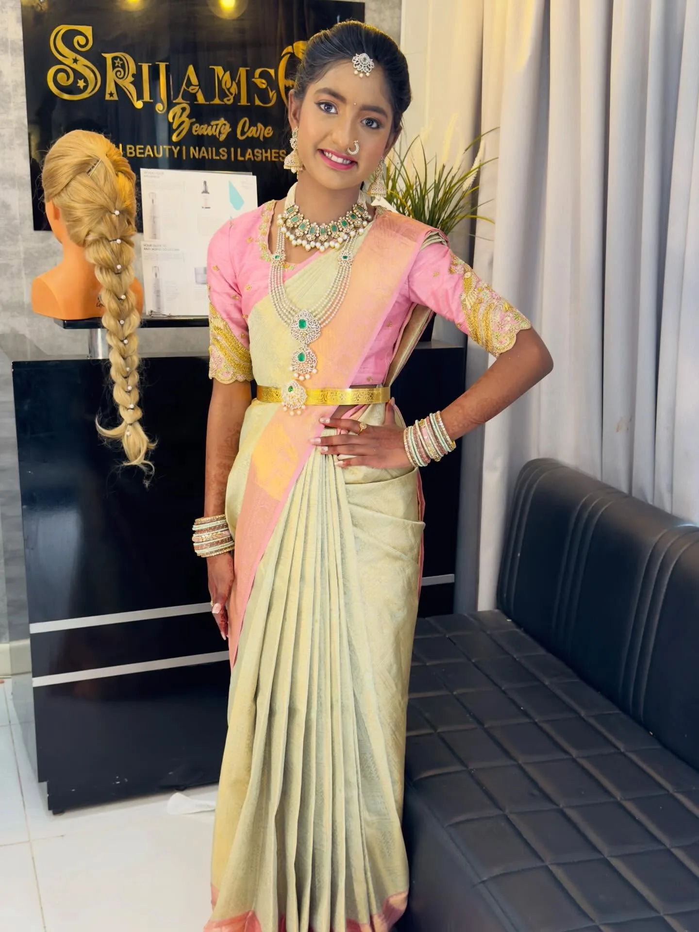 Teen client in cream and pink half-saree with green jewellery, standing by the Srijams plaque