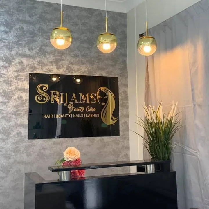 Srijams Beauty Care reception — gold illuminated plaque on warm-grey wall, three gold-globe pendant lights, black counter with roses